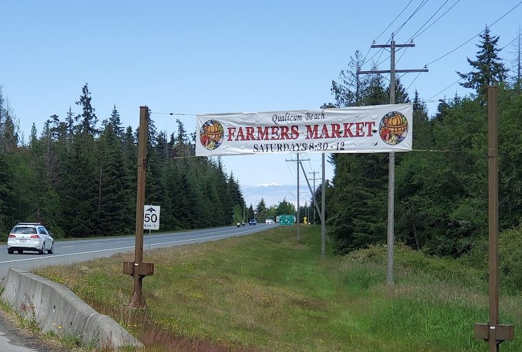 A banner hanging between two telephone poles above a road, with cars driving underneath. The banner reads