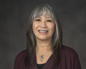 Councillor Young is pictured in front of a dark grey background. Her hair is down and comes to her shoulders. She wears a dark purple blouse and a silver necklace.